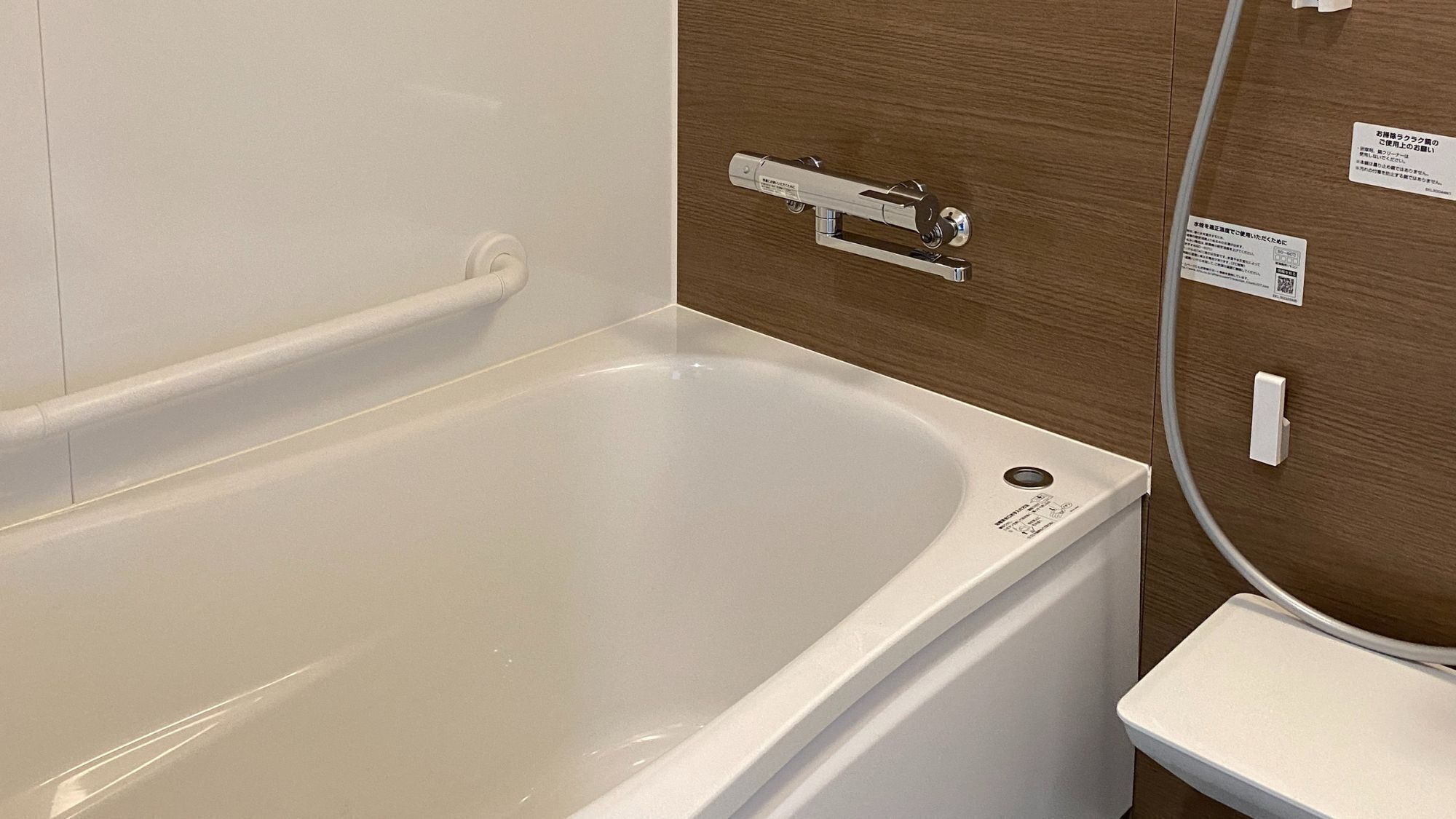 Une baignoire blanche dotée d’un siège intégré, d’une barre d’appui et d’un panneau de commande fixé au mur.