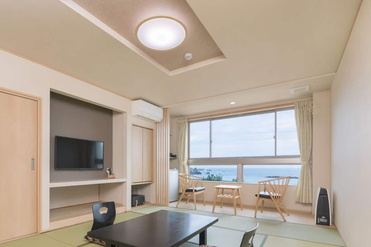 Una habitación con televisión, una mesa, sillas, un ventanal con vistas y una lámpara en el techo.