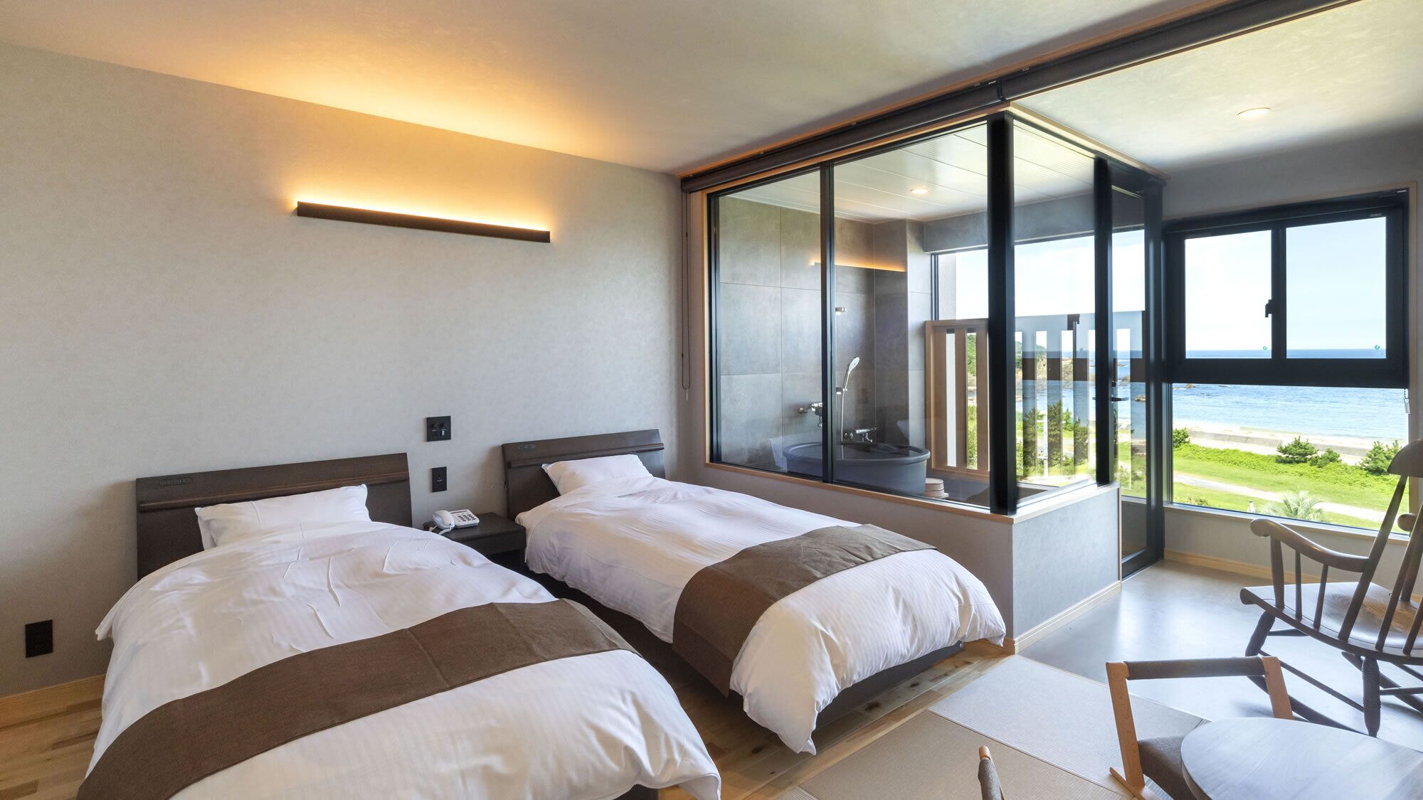 Une chambre d’hôtel moderne avec deux lits, une grande fenêtre donnant sur la mer et un balcon.