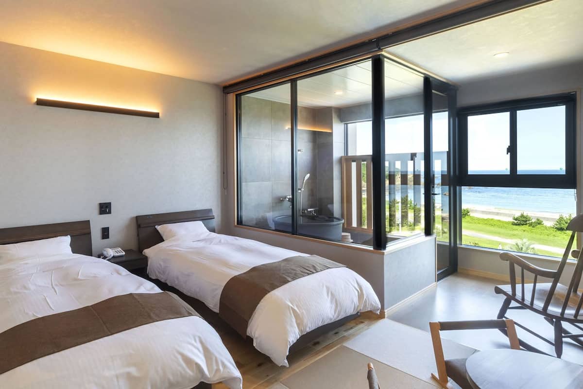Habitación de hotel moderna con dos camas, un ventanal con vistas al mar y un balcón con una silla.