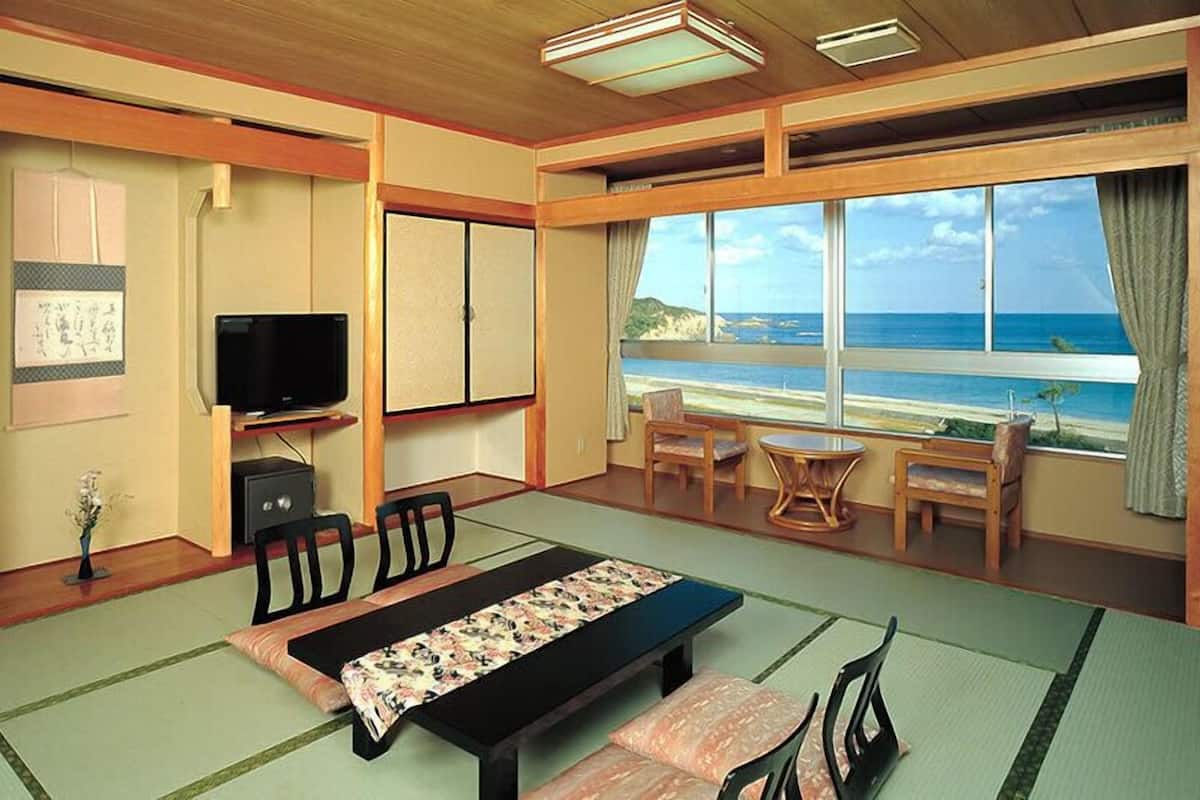 Una habitación con esteras de tatami, televisión, escritorio y vista al océano.