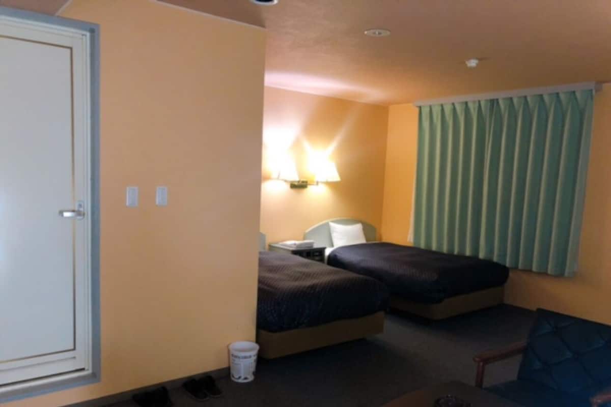 Habitación de hotel con dos camas, un escritorio, una silla, una lámpara y una ventana con cortinas.