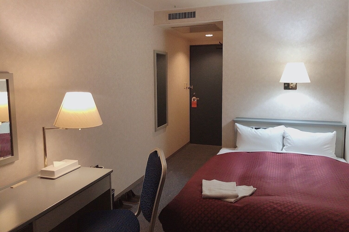 Habitación de hotel con cama, escritorio con lámpara, silla y puerta que da a otra habitación.