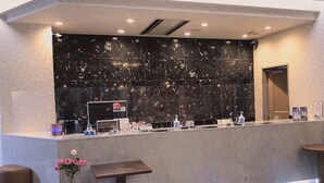 Zona d'estació amb paret de marbre, taulell de recepció i zona de seients amb un ram de flors.