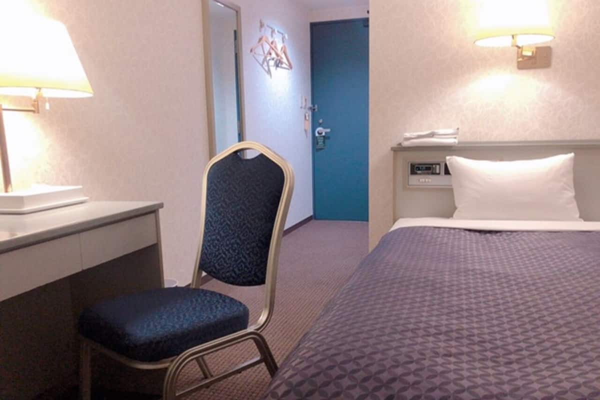 Una habitación de hotel con una cama, un escritorio, una silla y una puerta.