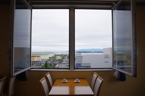 Une pièce avec une table et des chaises, une grande fenêtre donnant sur la ville et une vue sur les montagnes au loin.