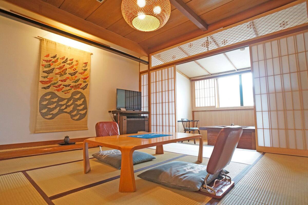 Um quarto japonês tradicional com tatames, uma mesa baixa, uma televisão e portas deslizantes.