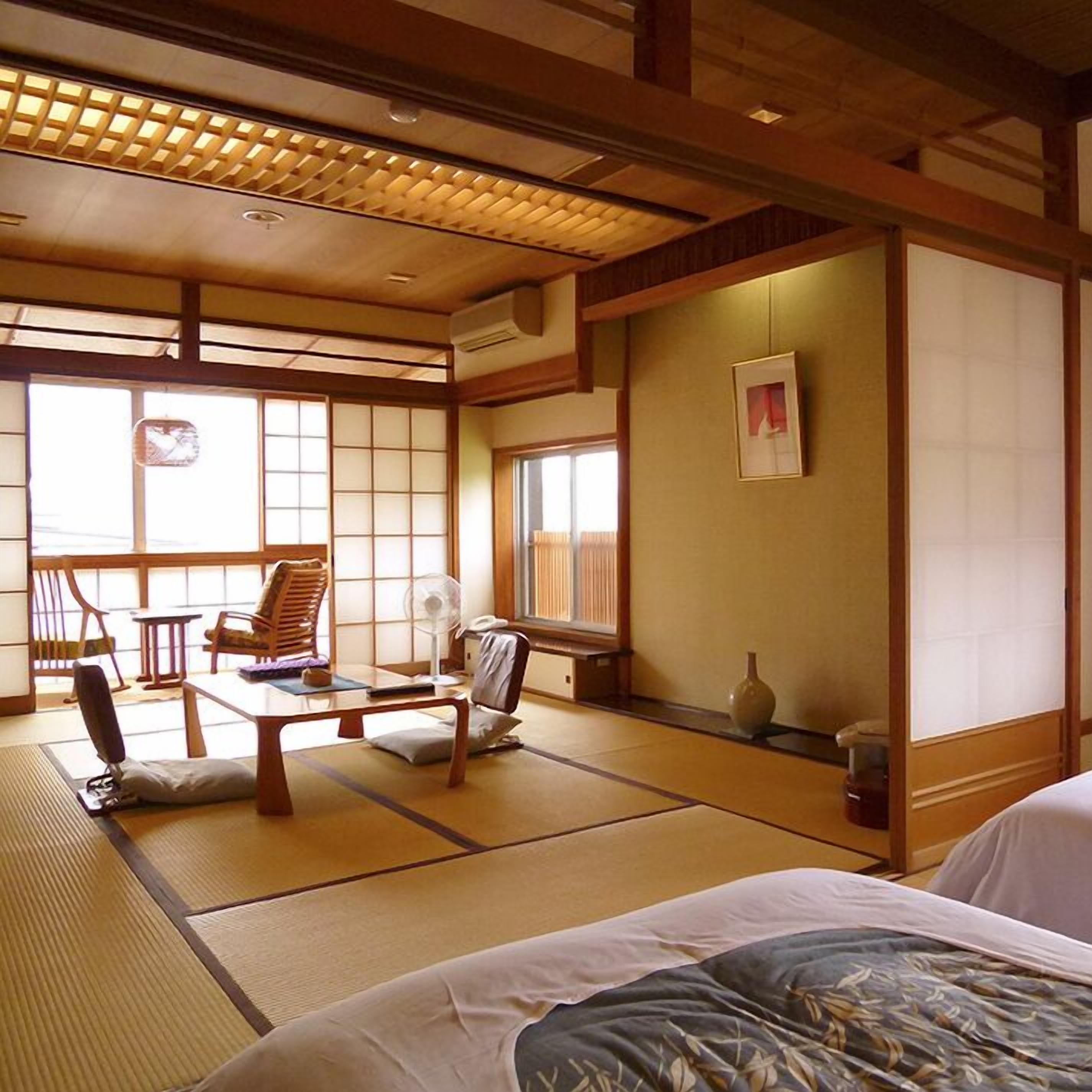 A traditional Japanese room with tatami flooring, a low table, chairs, and a bed.