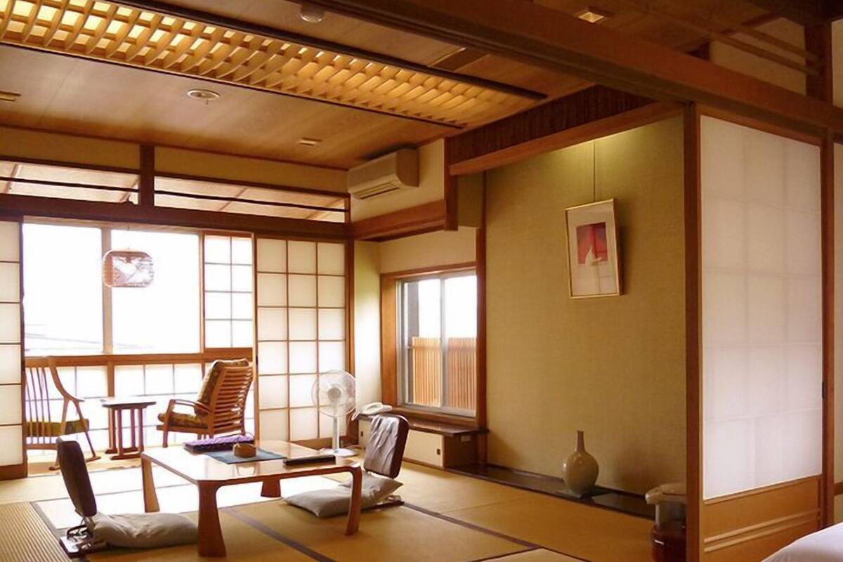 Um quarto japonês tradicional com tatames, uma mesa baixa, cadeiras e uma cama.