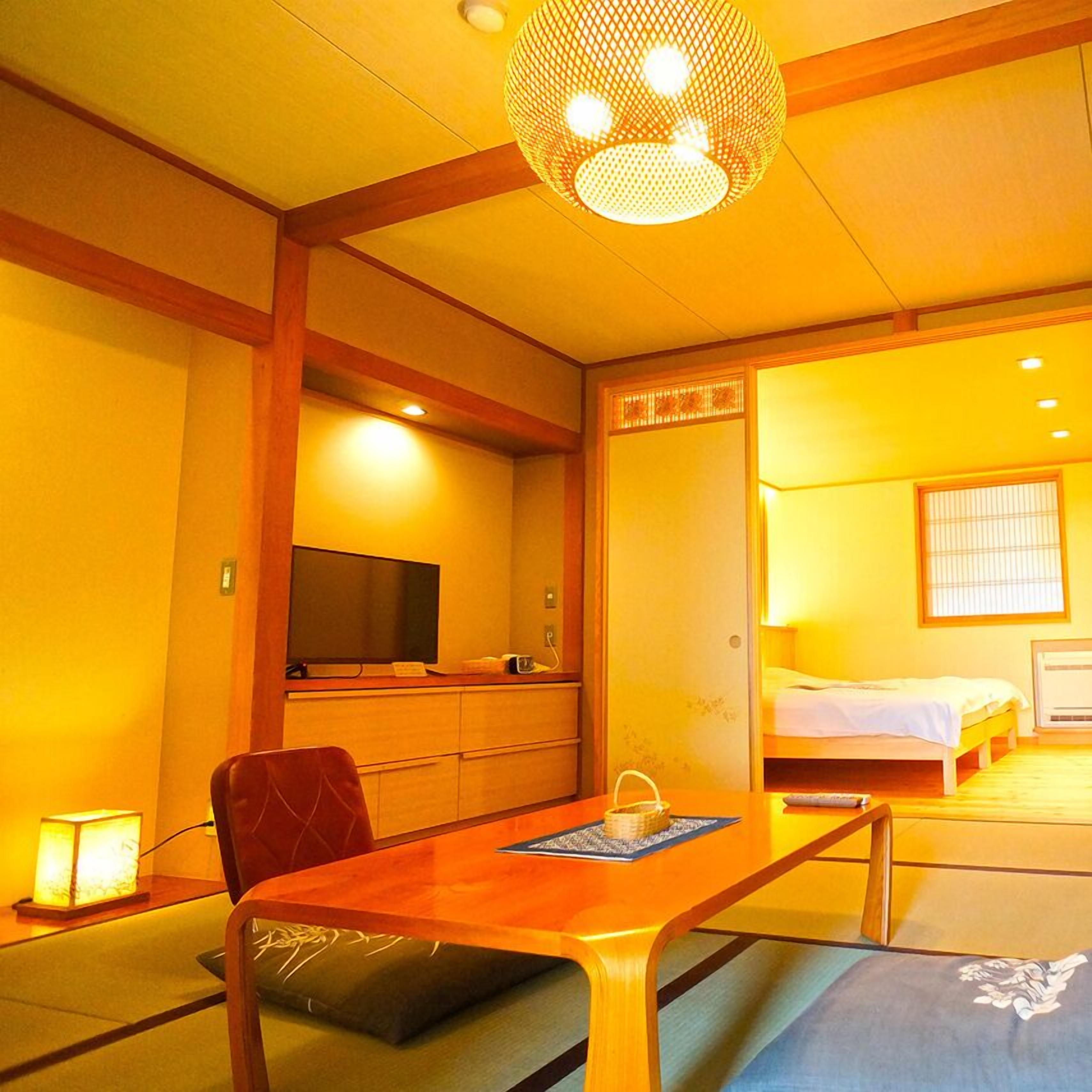 A traditional Japanese-style room with tatami flooring, a low wooden desk, a bed, and a television.