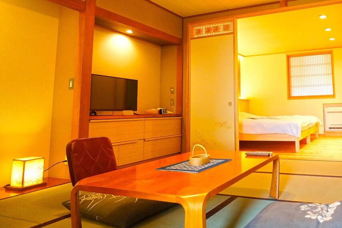 Um quarto tradicional japonês com tatames, uma mesa de madeira baixa, uma cama e uma televisão.