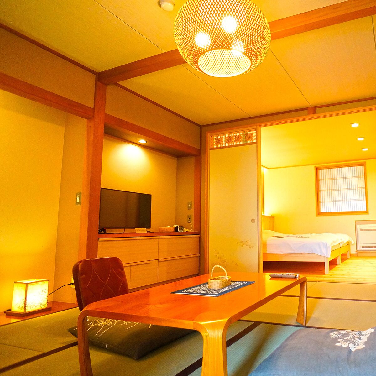 A traditional Japanese-style room with tatami flooring, a low wooden table, a television, and a bed with a futon.