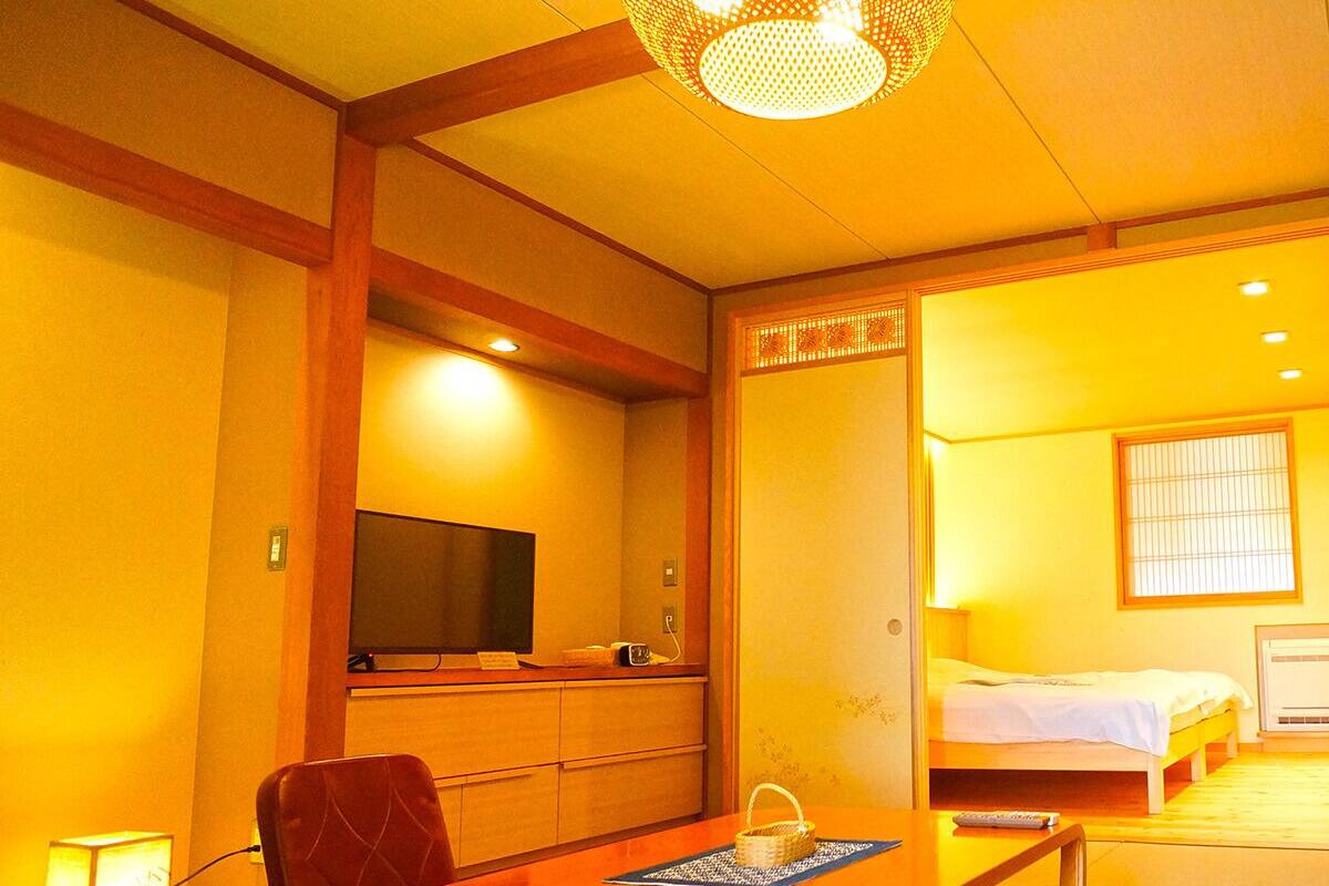 Um quarto tradicional japonês com piso de tatame, uma mesa de madeira baixa, uma televisão e uma cama com futon.