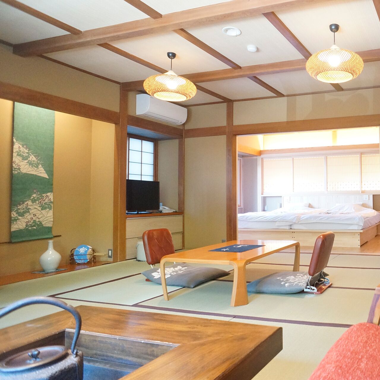 A traditional Japanese-style room with tatami flooring, a low wooden table, a television, and a bed with a futon.