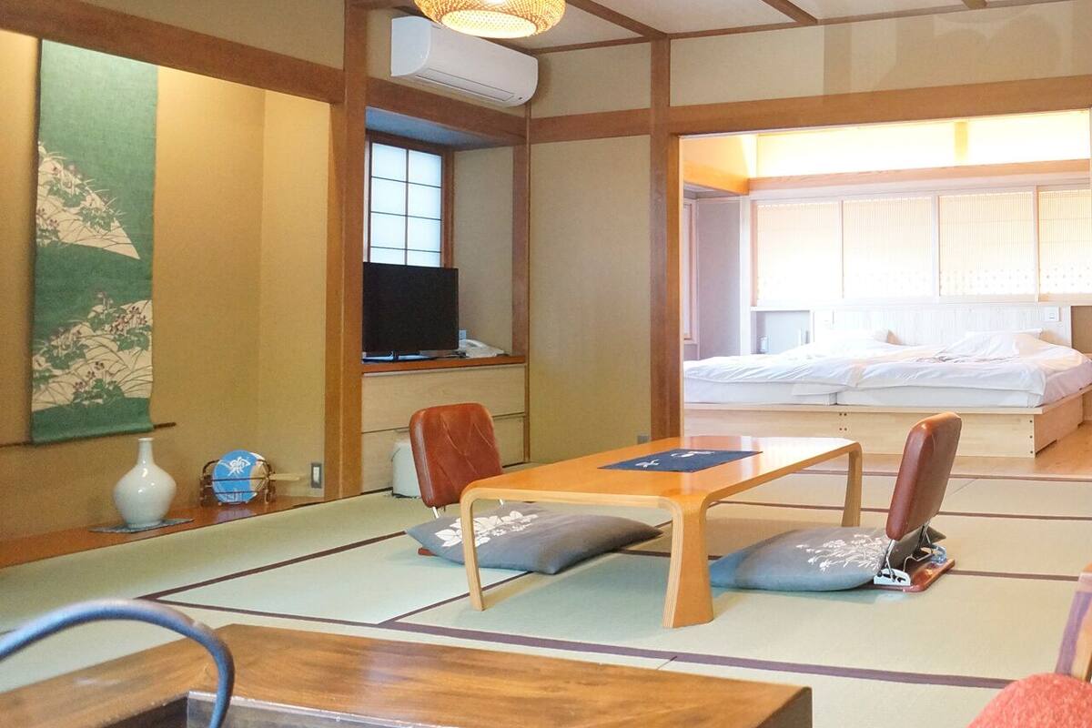 Um quarto em estilo japonês tradicional, com tatames, uma mesa de madeira baixa, uma televisão e uma cama com futon.