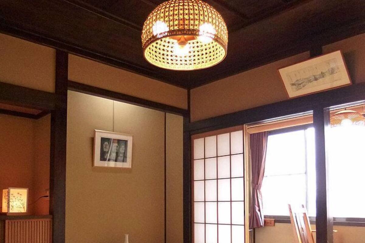 Um quarto japonês tradicional com tatames, uma mesa baixa, uma poltrona acolchoada, um candeeiro pendente e um painel deslizante shoji.