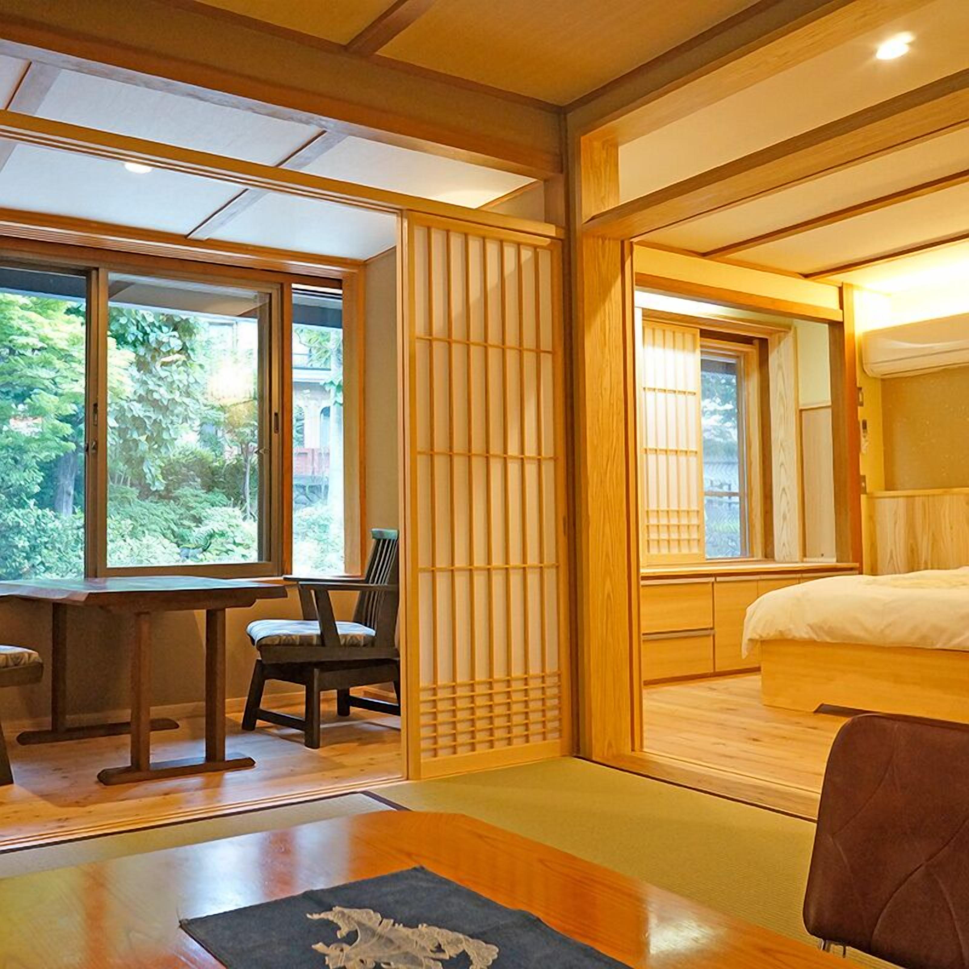 A traditional Japanese-style room with tatami flooring, a low table with a chair, a bed with a wooden headboard, and sliding doors with shoji screens.