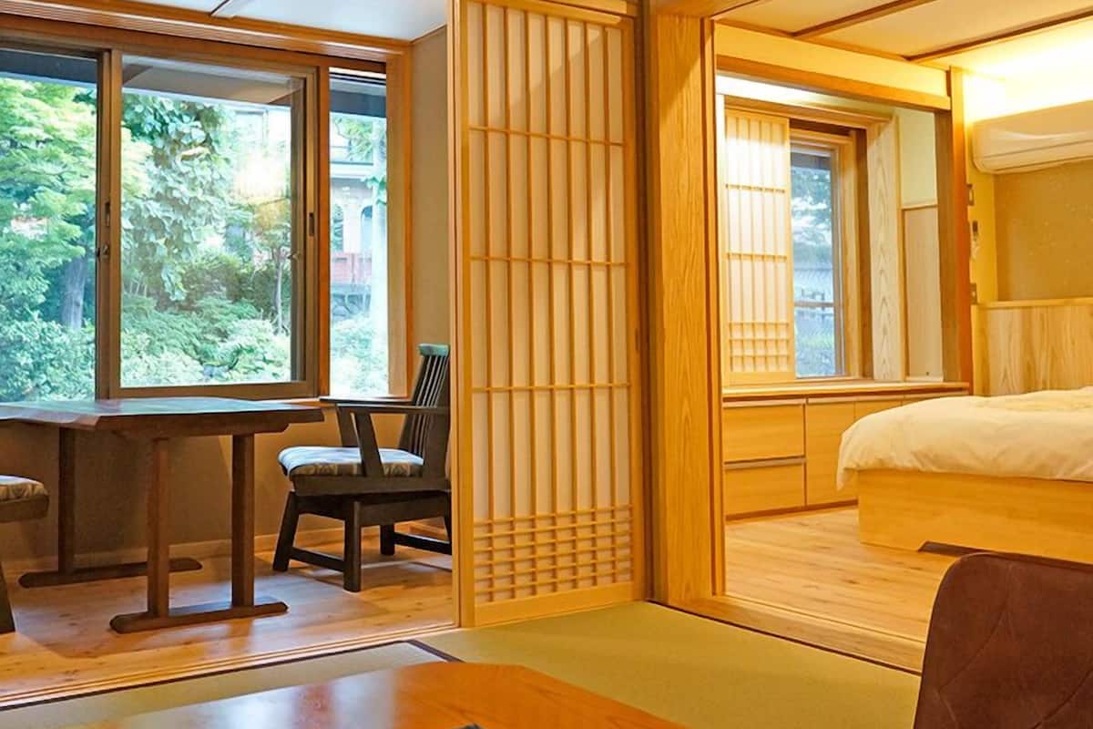 A traditional Japanese-style room with tatami flooring, a low table with a chair, a bed with a wooden headboard, and sliding doors with shoji screens.