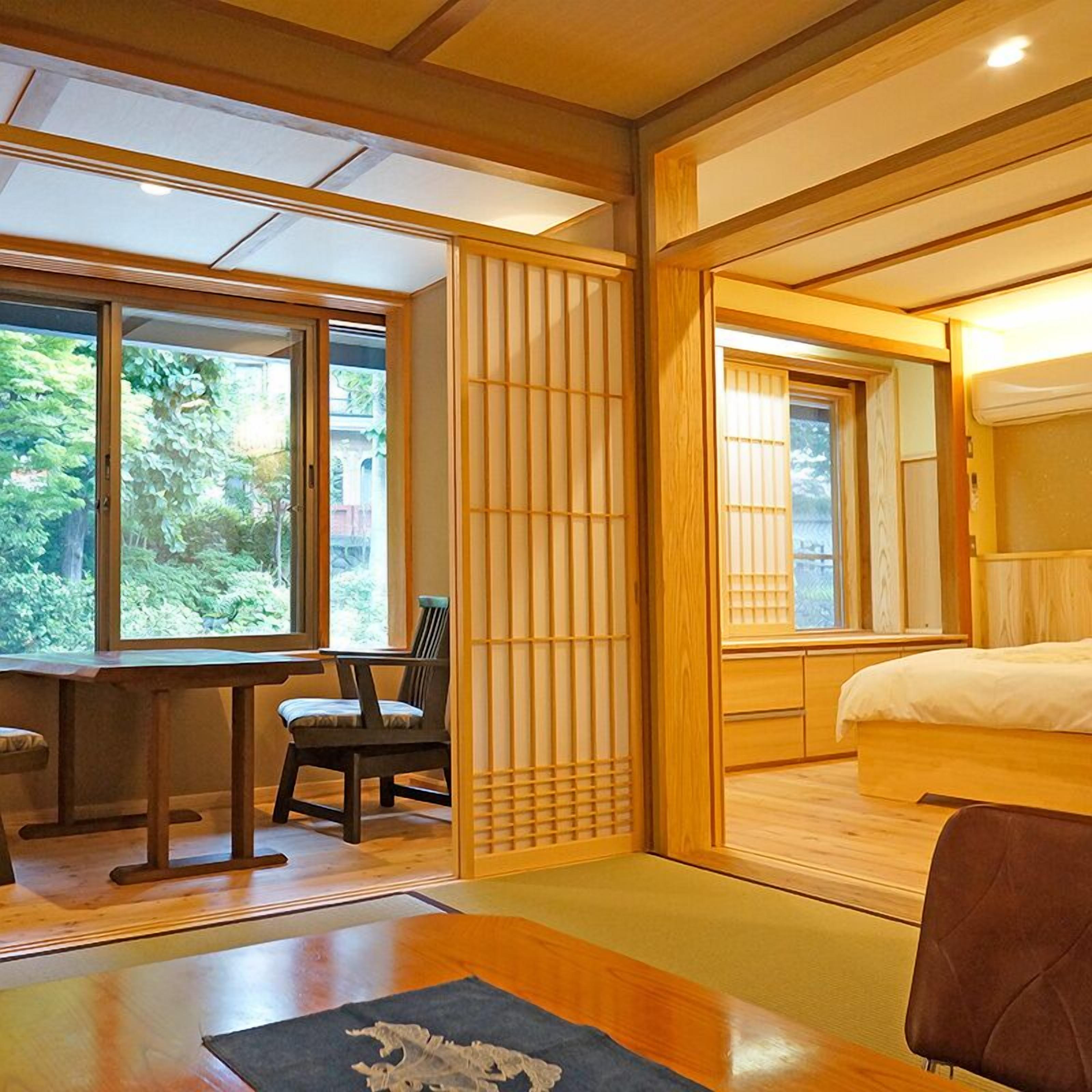 A traditional Japanese-style room with tatami flooring, a low wooden bed, a desk with a chair, and sliding shoji screens.