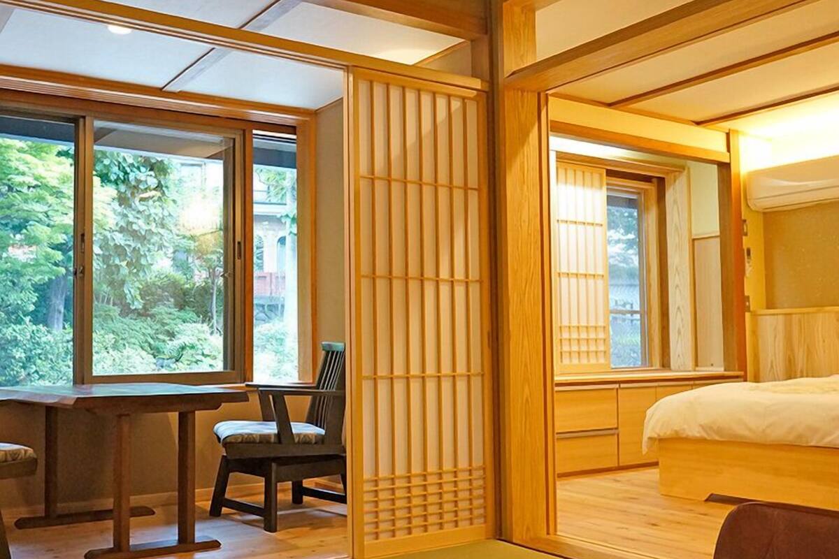 Um quarto em estilo japonês tradicional, com tatames, cama de madeira baixa, escrivaninha com cadeira e portas corrediças shoji.