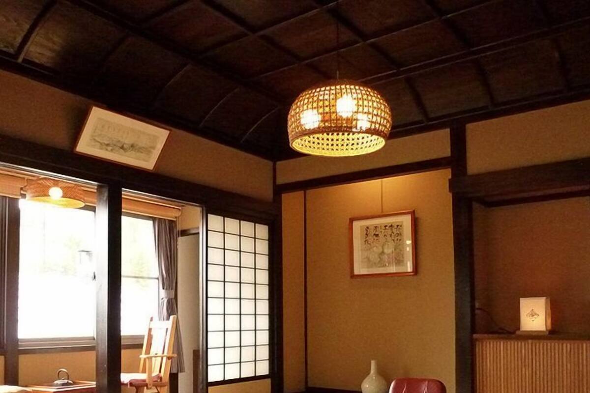 Um quarto japonês tradicional com tatames, uma mesa de madeira baixa, uma cadeira almofadada, um candeeiro pendente e uma porta de tela shoji.