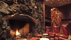 Un vestíbulo con pared de piedra, chimenea, sillones de cuero y pequeñas mesas.