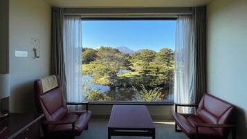 A room with two leather chairs, a small table, and a large window offering a view of a lake and trees.