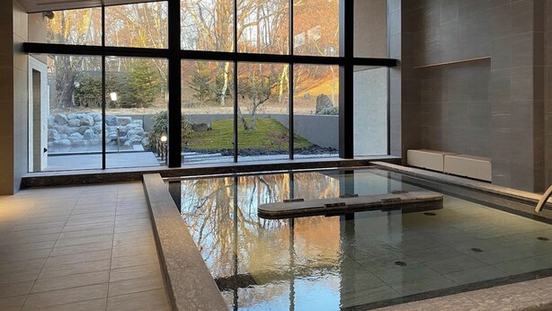 Una piscina interior moderna con amplios ventanales, un borde de piedra y vistas a un paisaje natural.