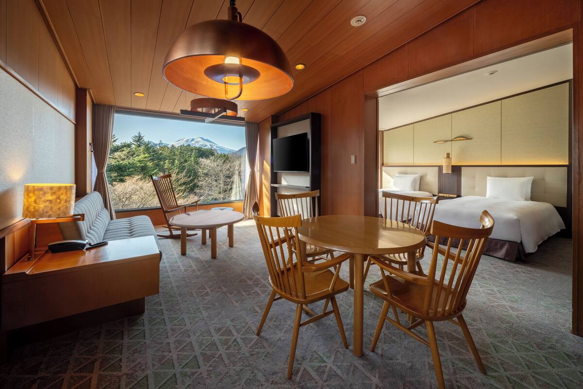 Camera d'hotel con un letto, una televisione, un'area pranzo con sedie e un tavolo, e vista su una montagna.