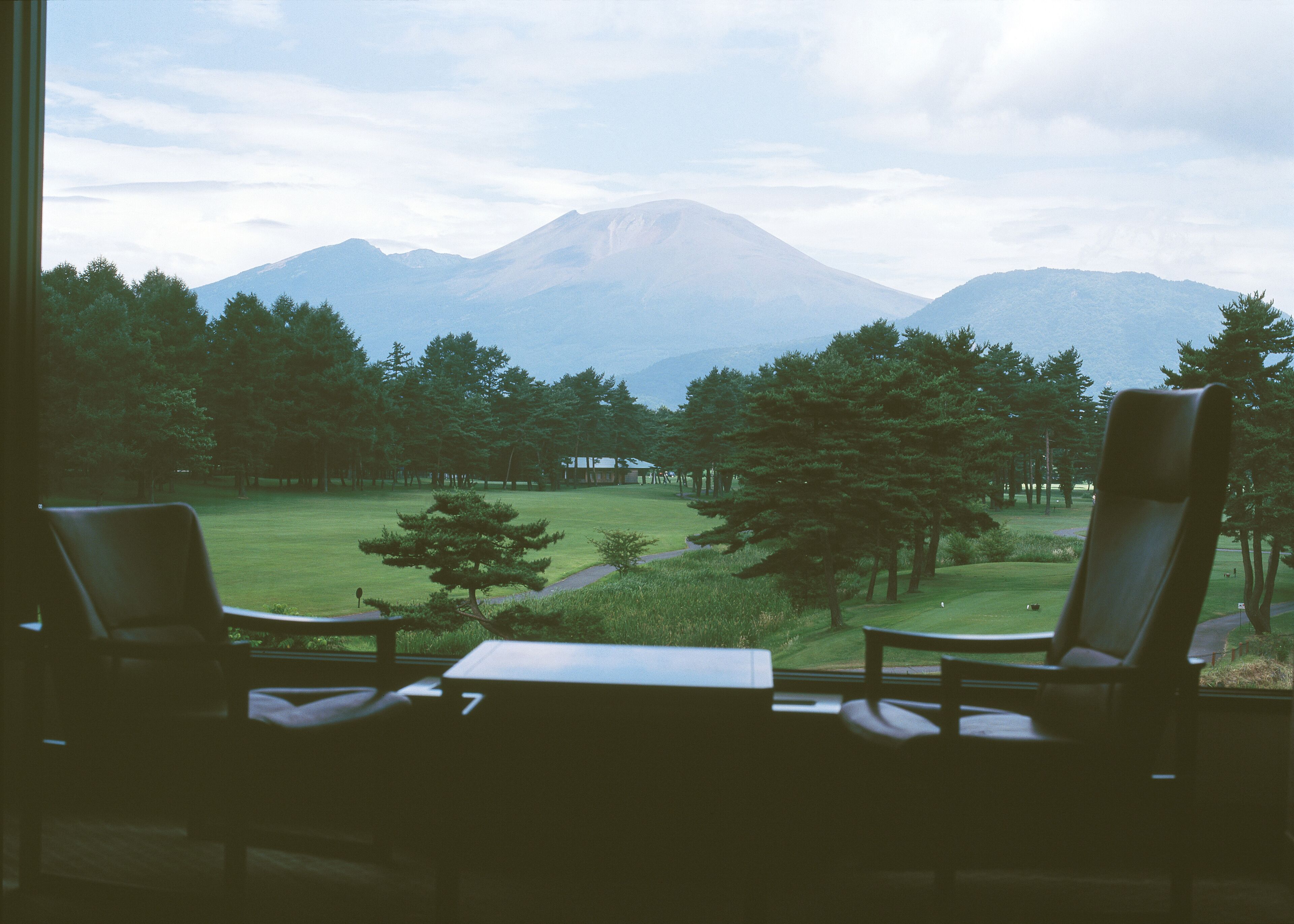 Une pièce avec deux fauteuils placés face à une vue sur une montagne et un parc.