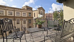Um terraço com mesa e cadeiras de metal, um vaso de planta e um lustre.