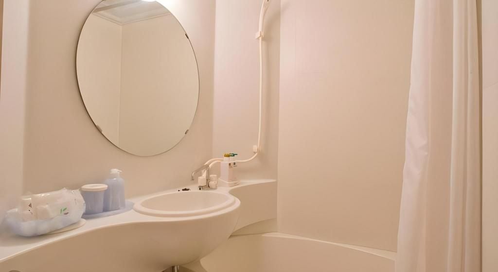 Un baño con un espejo redondo, un lavamanos y una zona de ducha.