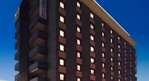 A multi-story hotel building with a modern design, featuring a series of balconies on the left side and a row of windows on the facade.