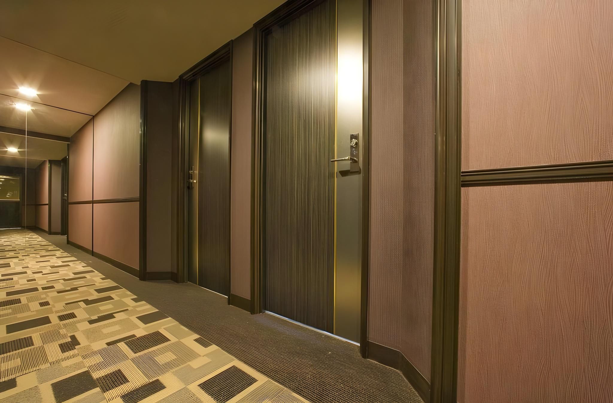 A hotel corridor with closed doors, a patterned carpet, and a wall-mounted light fixture.