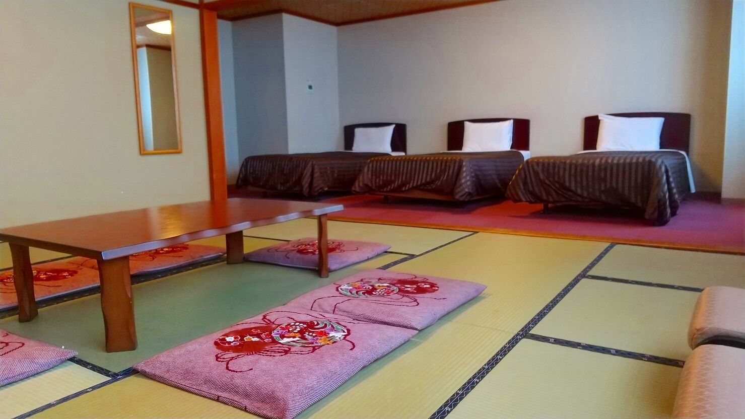 Quarto com esteiras de tatame, uma mesa de madeira e três camas com roupa de cama escura.