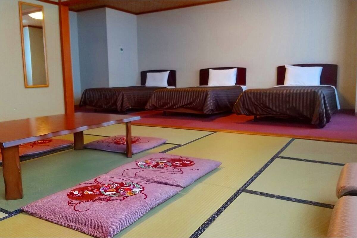 Una habitación con tatamis, una mesa de madera y tres camas con ropa de cama oscura.
