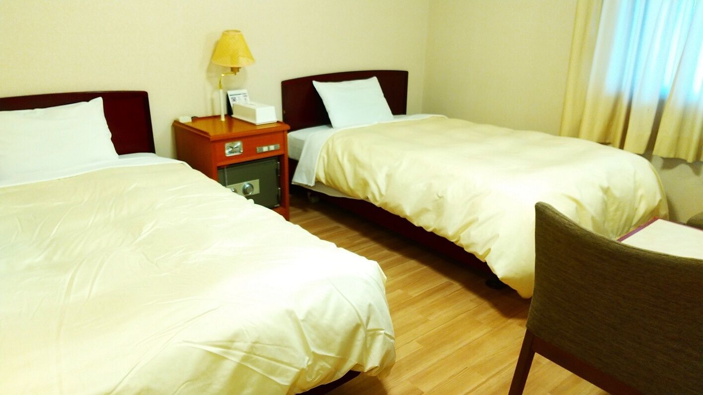 Habitación de hotel con dos camas, una mesita de noche con una lámpara y una silla.