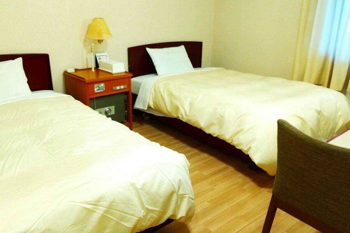 Habitación de hotel con dos camas, una mesita de noche con una lámpara y una silla.
