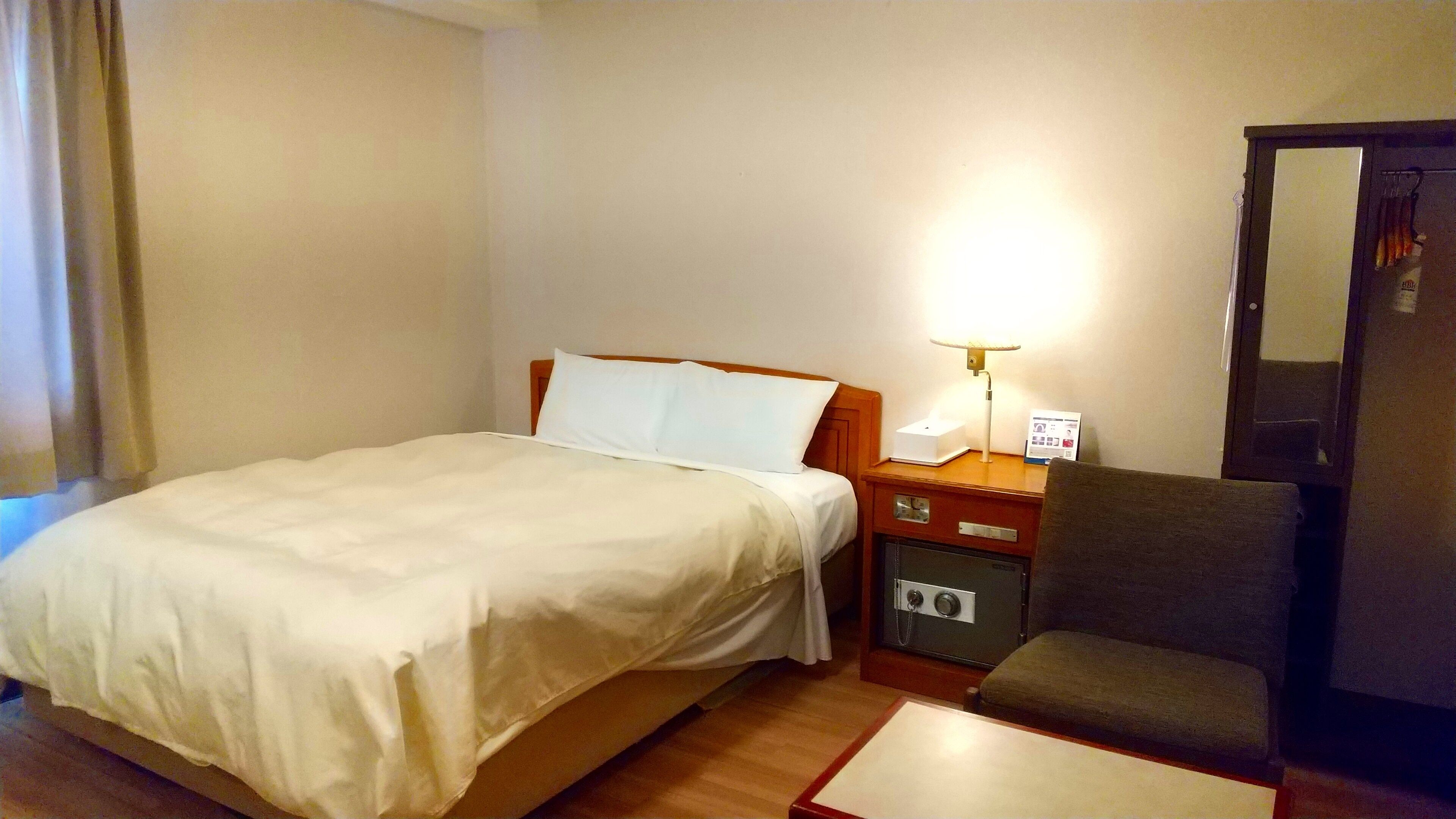Quarto de hotel com cama, escrivaninha com luminária, cadeira e guarda-roupa.