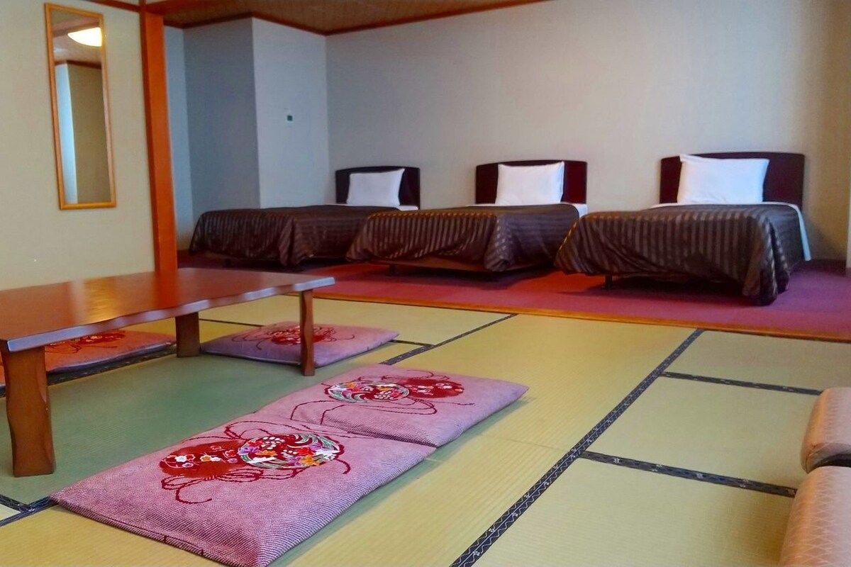 A room with tatami mats, a wooden table, and three beds with dark bedding.