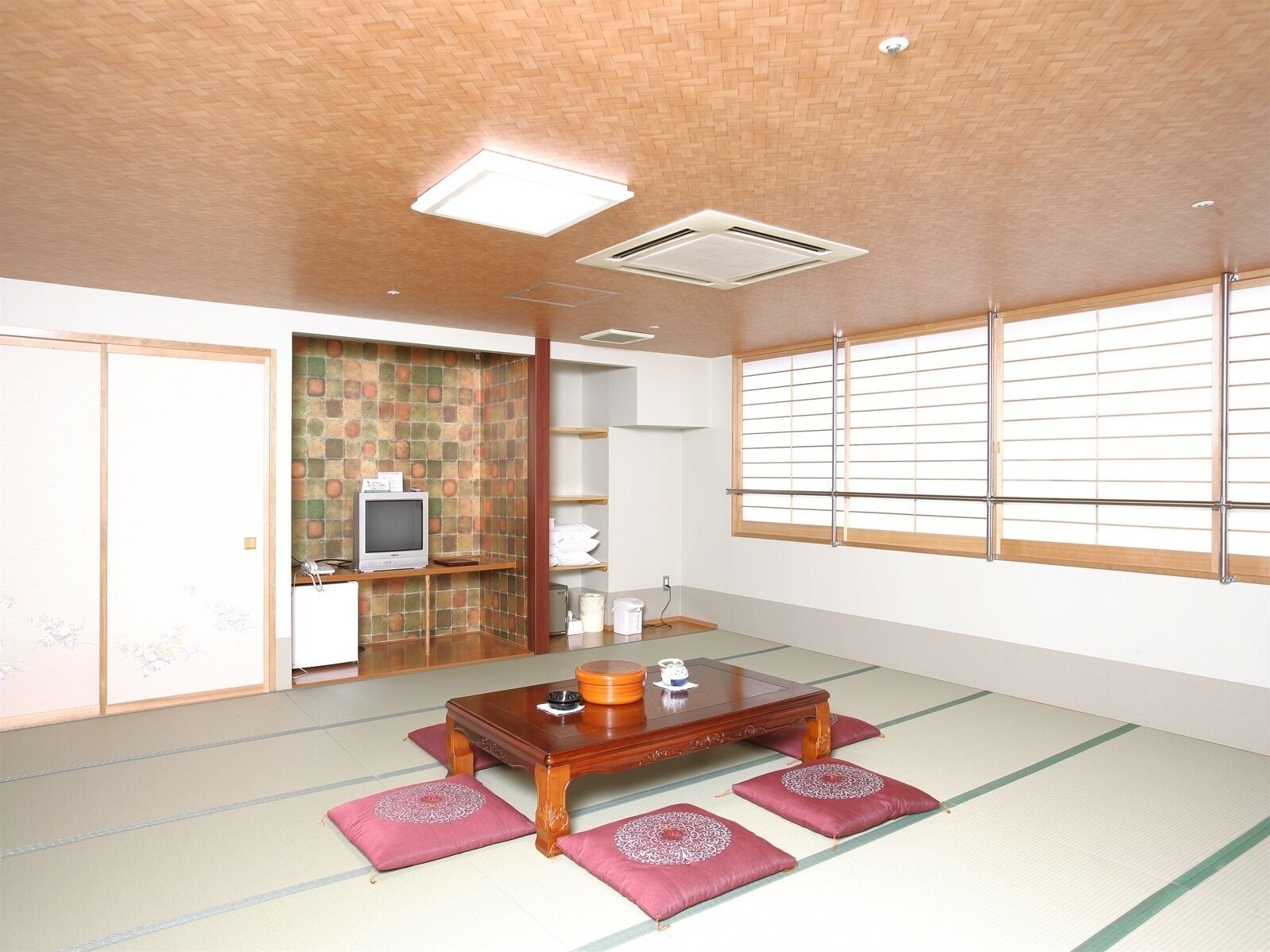 Quarto tradicional japonês com tatames, uma mesa de madeira baixa, uma televisão e portas deslizantes.