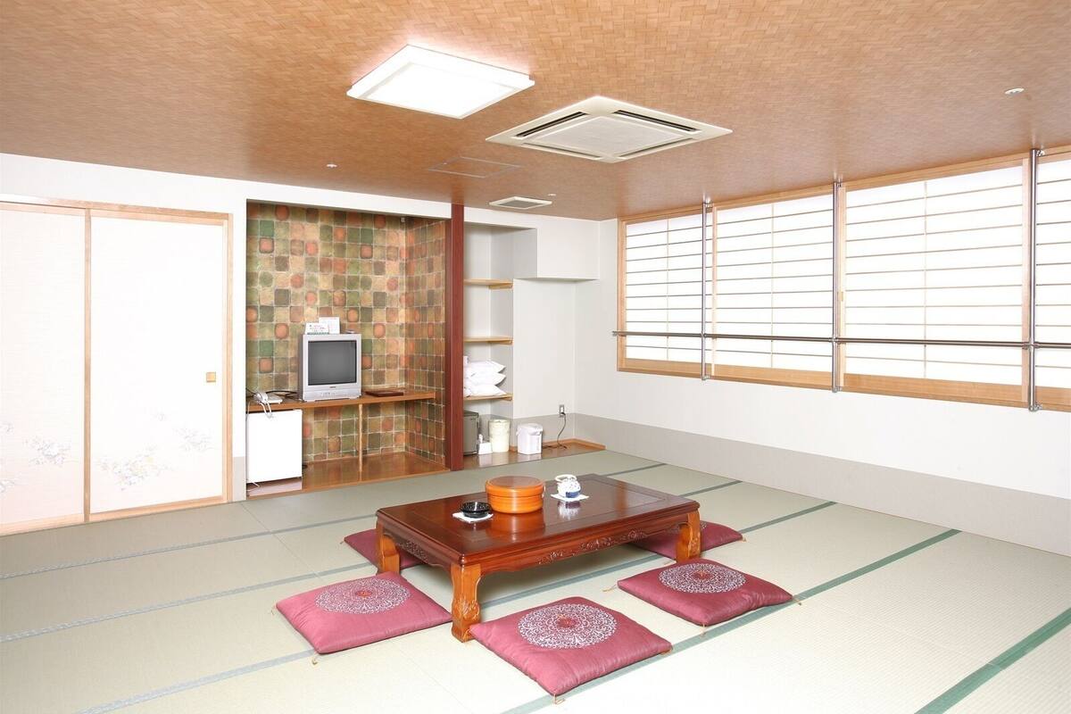 Una habitación tradicional japonesa con suelo de tatami, una mesa de madera baja, un televisor y puertas correderas.