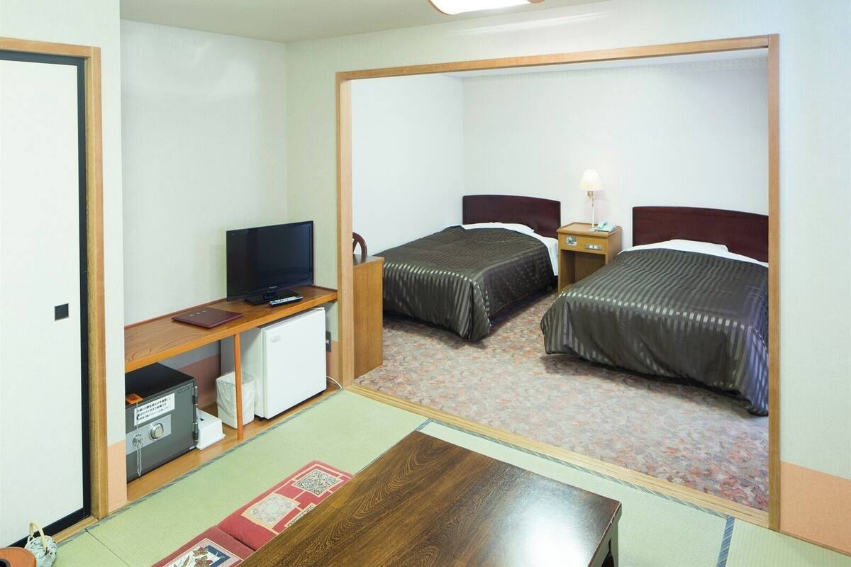 Habitación de hotel con dos camas, un escritorio con televisor, un refrigerador pequeño y una mesita de noche con lámpara.