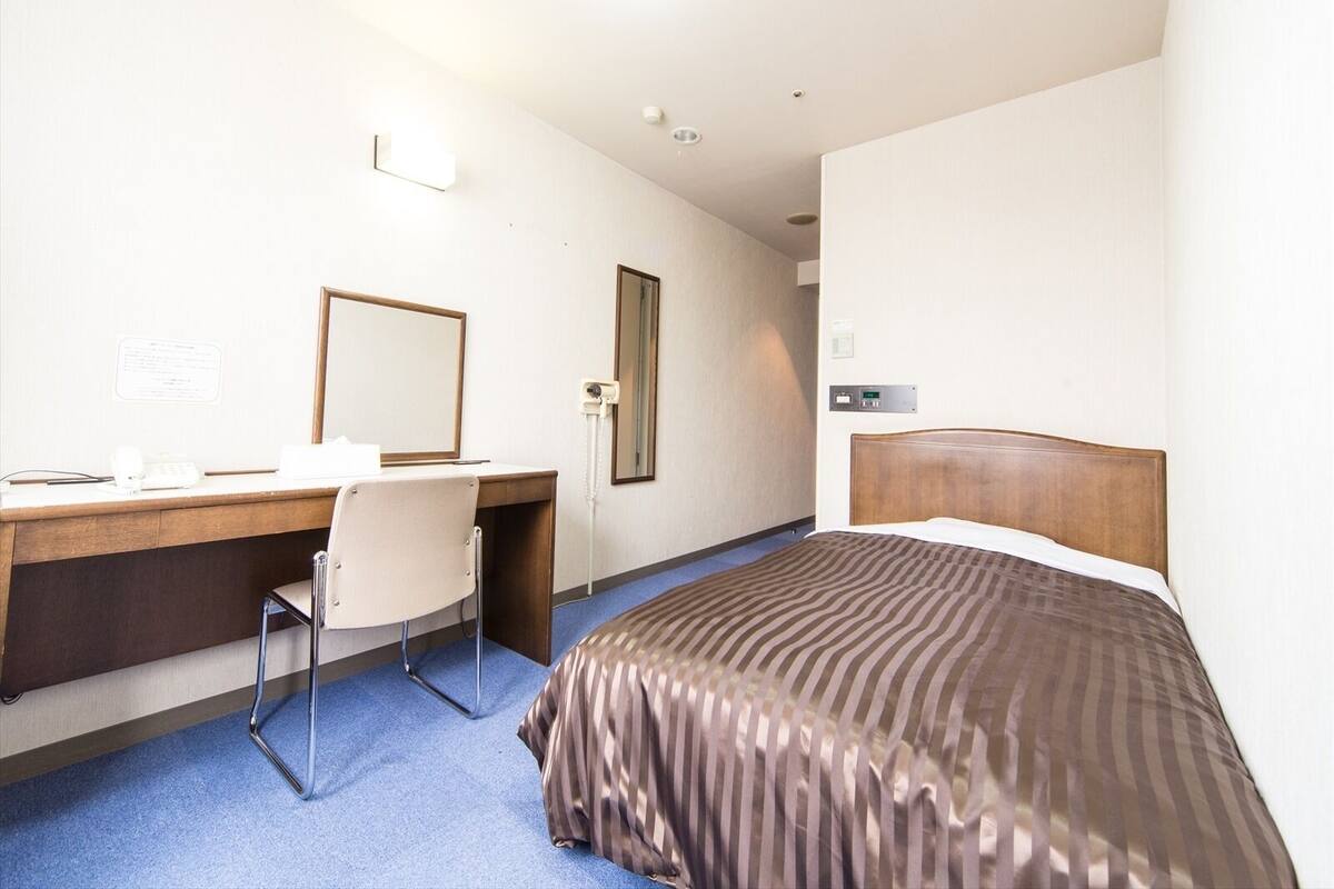 Habitación de hotel con cama, escritorio, silla, espejo, teléfono y panel de control en la pared.