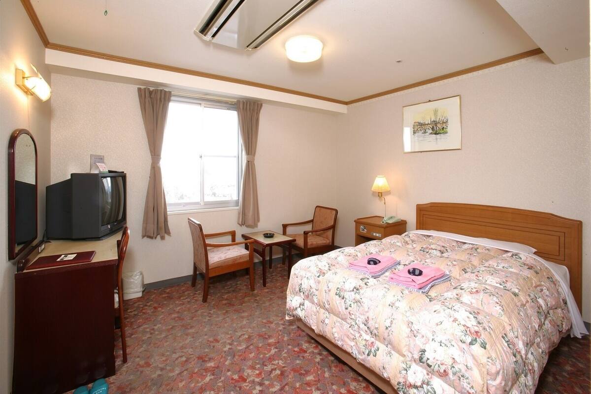 Una habitación de hotel con cama, escritorio, silla, televisión y un cuadro en la pared.