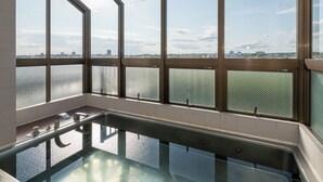 A modern indoor pool with large windows offering views of a cityscape and a body of water. - Business Hotel Koyo (Aichi)