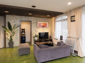 A modern living room with a flat-screen TV, grey sofas, a large potted plant, and a decorative wall panel. - Business Hotel Koyo (Aichi)