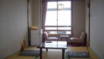 A traditional Japanese room with tatami flooring, a low table, two chairs, a small table, and a window with a view.