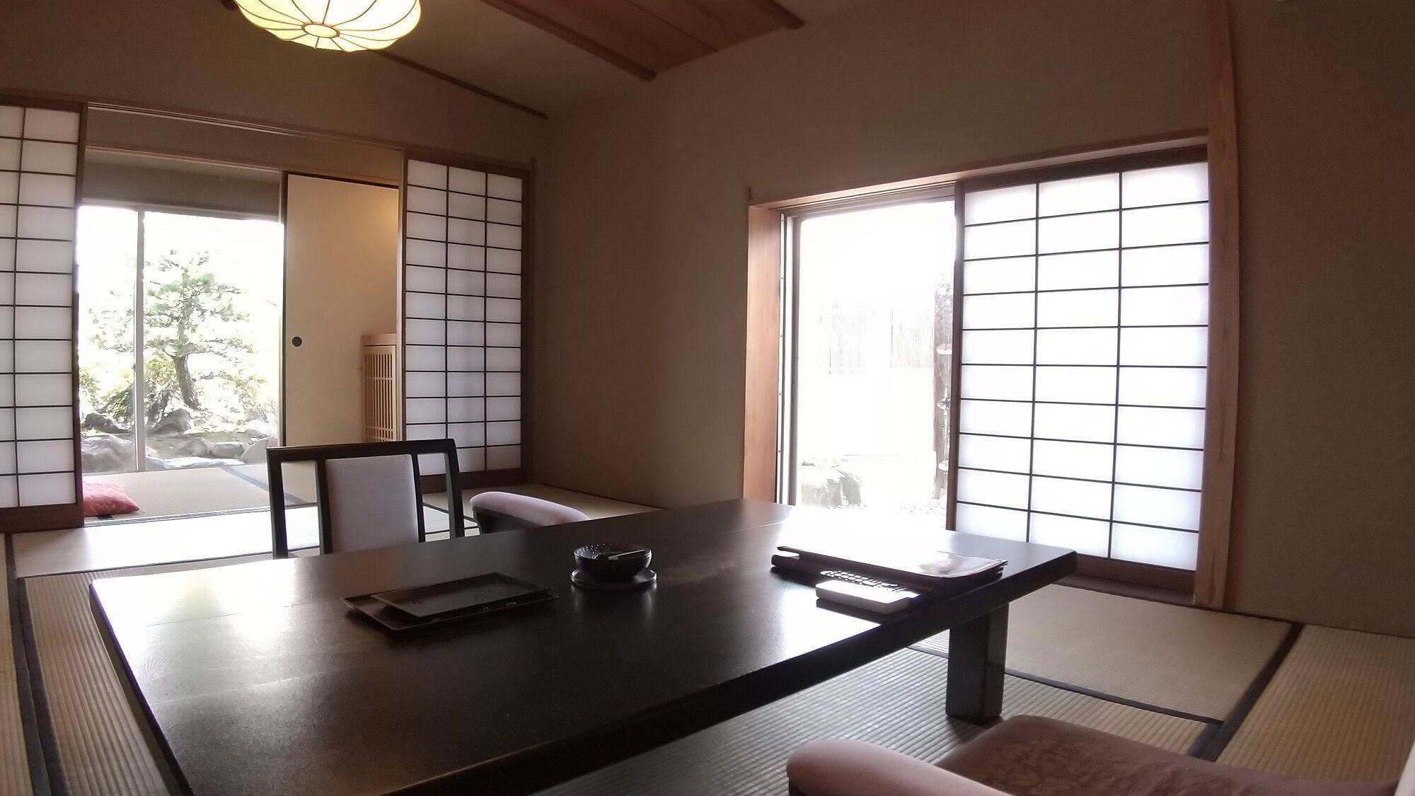 A traditional Japanese room with tatami flooring, a low table, a chair, and sliding doors with a view of a garden.