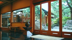 A traditional Japanese interior with tatami flooring, a wooden door leading to a garden, and a large vase with branches. - Atami Sekitei (Atami)